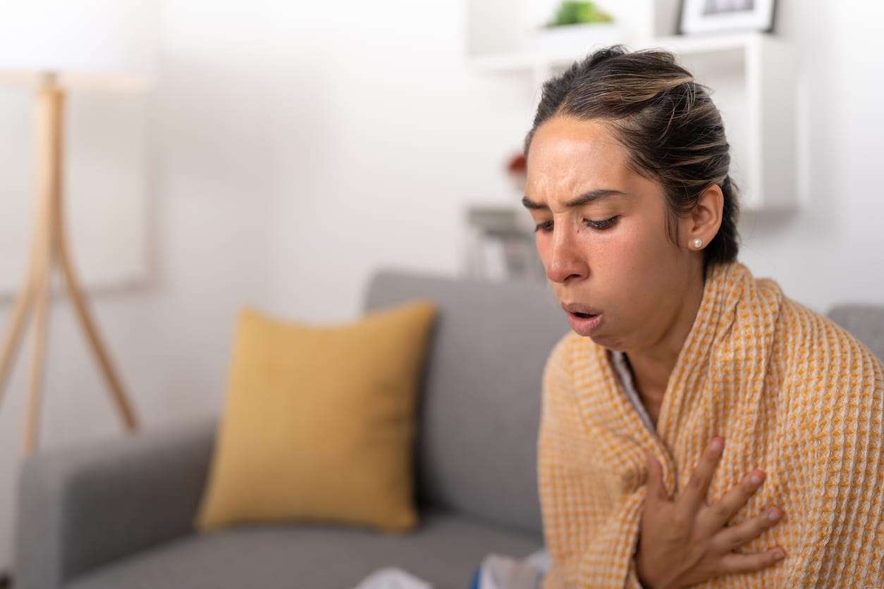 Sick woman coughing on the couch.