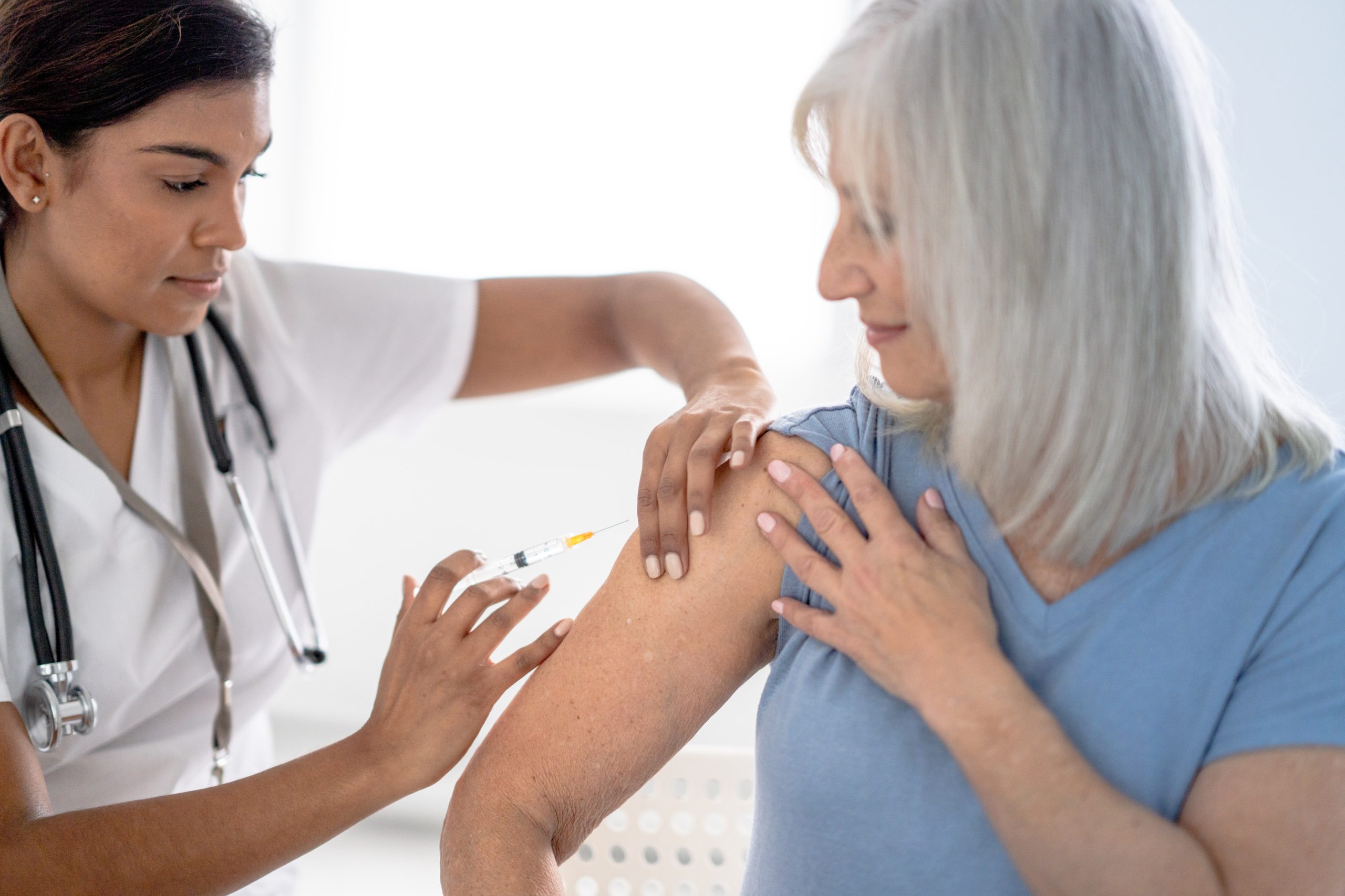 A woman confidently looks on as a medical professional injects her with a dose of vaccine.