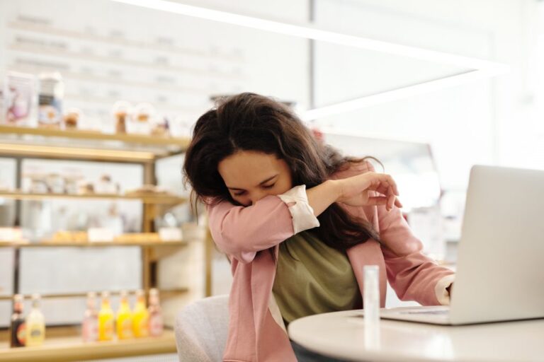 Woman covering a sneeze while working at a coffee shop.